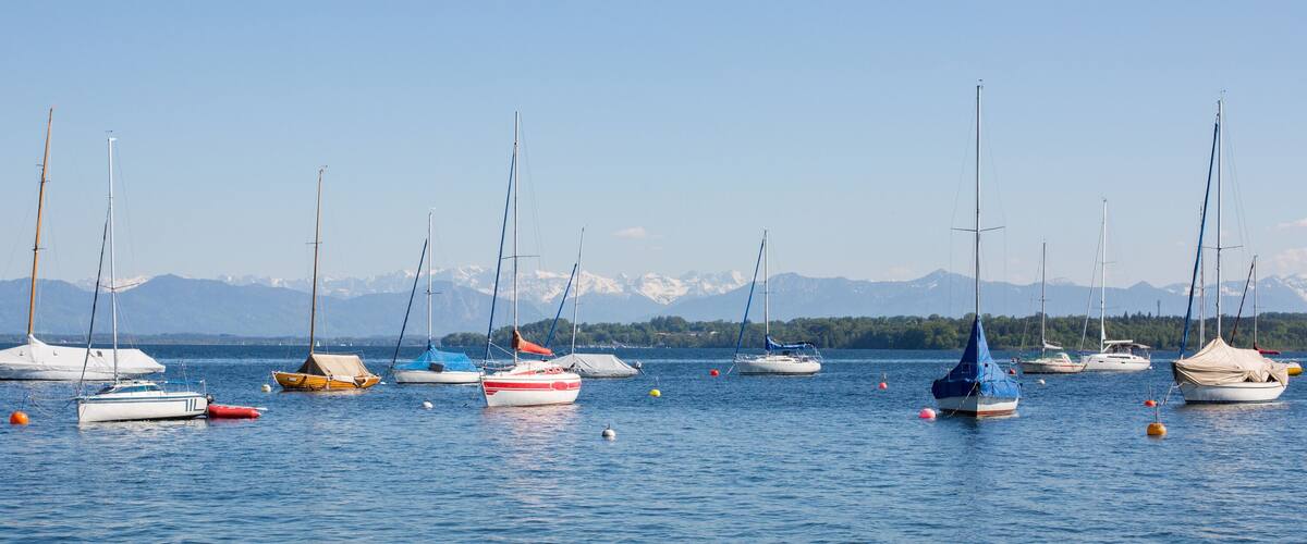 A calm lake with several sailboats anchored, surrounded by mountains and clear skies.