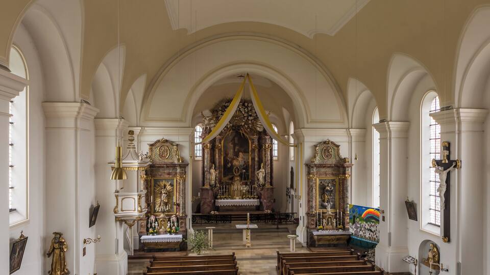 An ornate church interior with a central altar, pews, and religious statues.