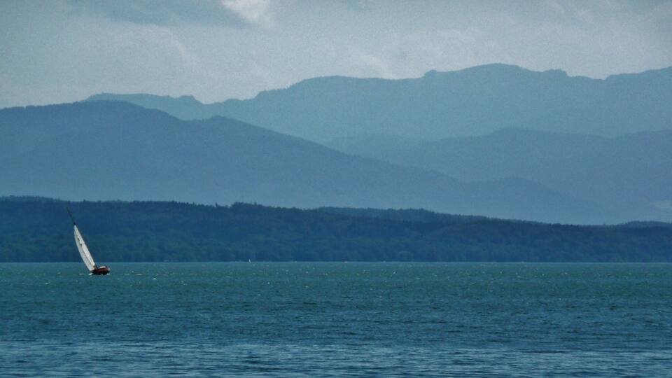 A sailboat on a calm sea with a forested mountain range in the background.