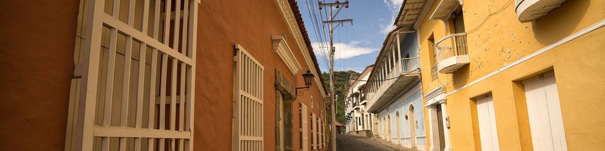 A cobblestone street flanked by buildings with white shutters and balconies.