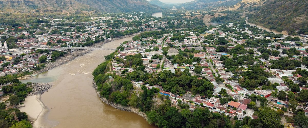 A river winding through a town with mountains in the background and a bridge crossing the river.