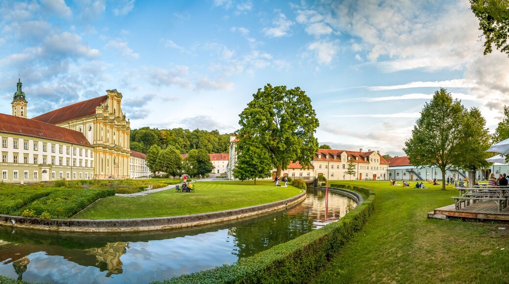 Ein historisches Gebäude mit rotem Dach, einem Kanal und gepflegten Gärten.