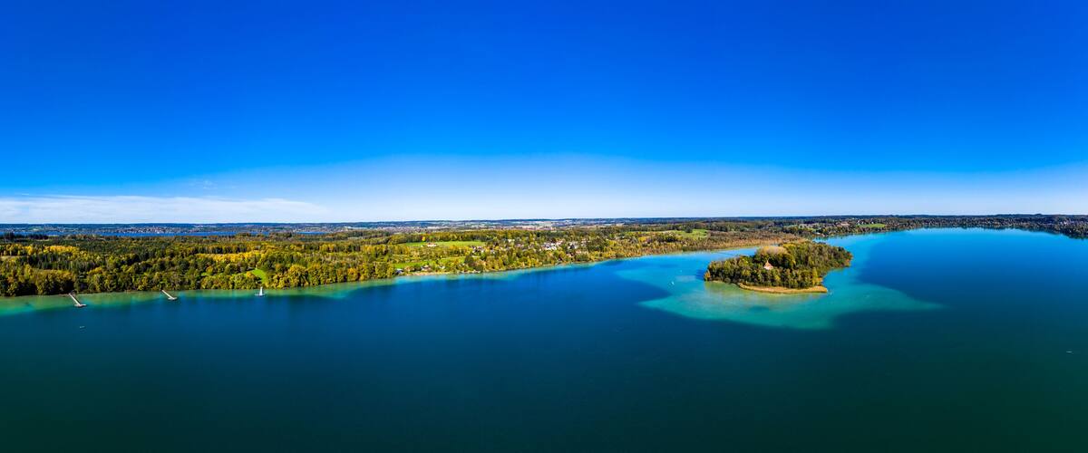 A panoramic view of a lake surrounded by dense forests and a small island with a lighthouse.