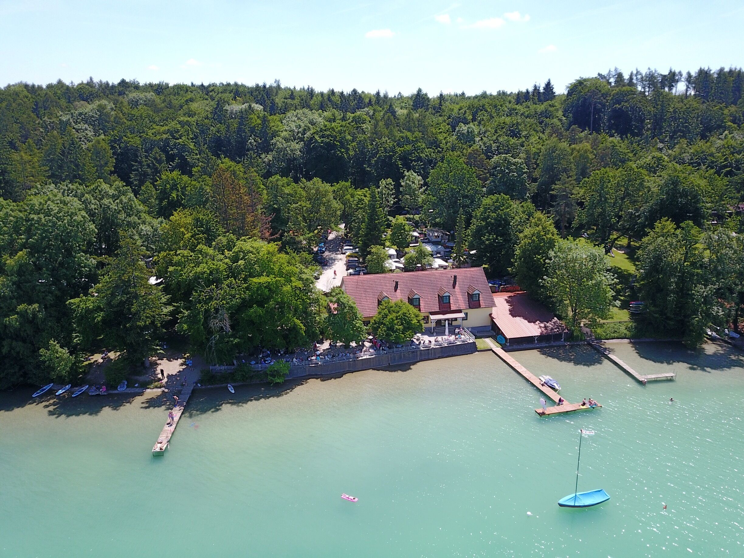 A lakeside property with a red-roofed building surrounded by dense trees.
