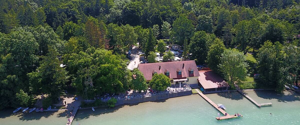 A lakeside property with a red-roofed building surrounded by dense trees.