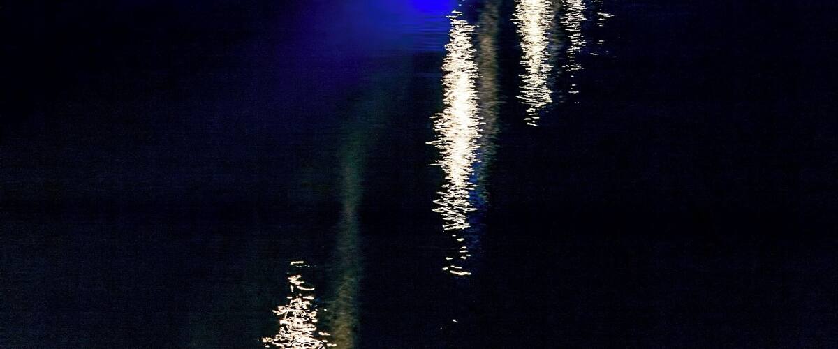 A bridge at night with blue and white lights reflecting on the water.