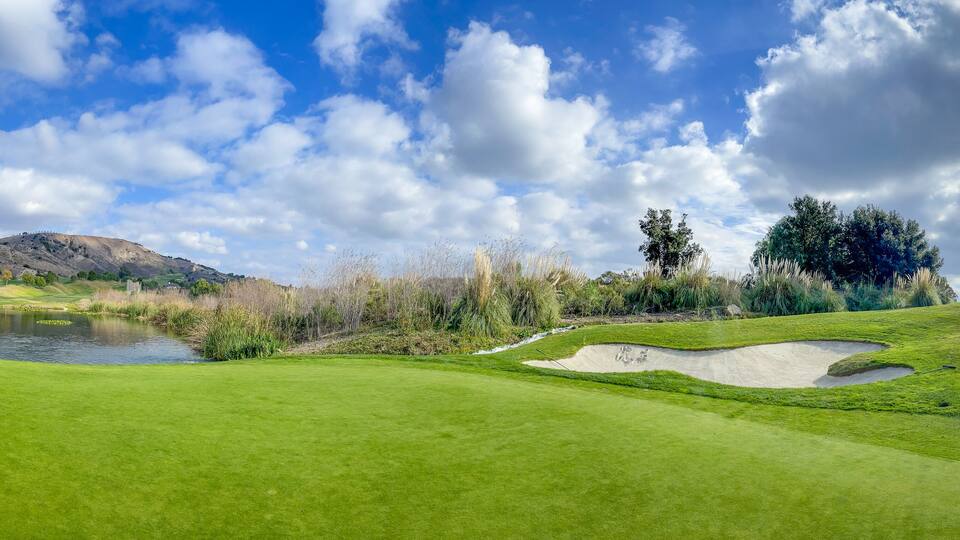 A golf course with a pond, sand bunkers, and a hilly landscape.