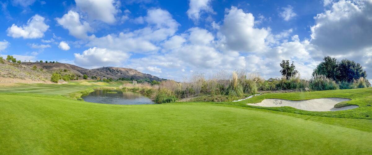A golf course with a pond, sand bunkers, and a hilly landscape.