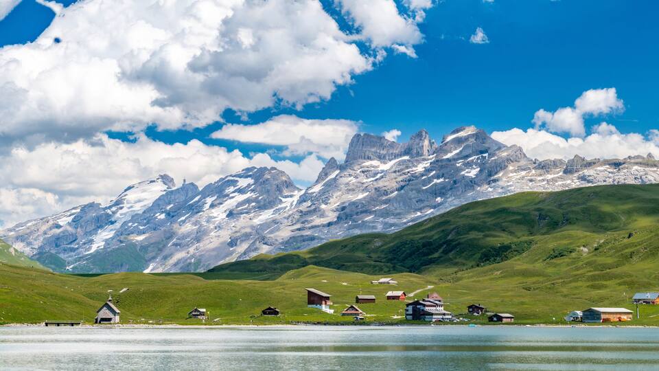 A lake surrounded by green hills and snow-capped mountains under a clear blue sky.