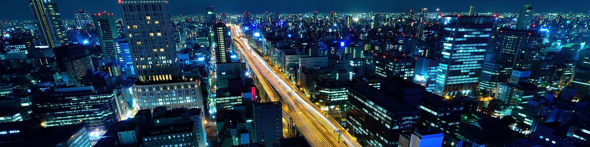 A nighttime cityscape with illuminated buildings and a multi-level highway.