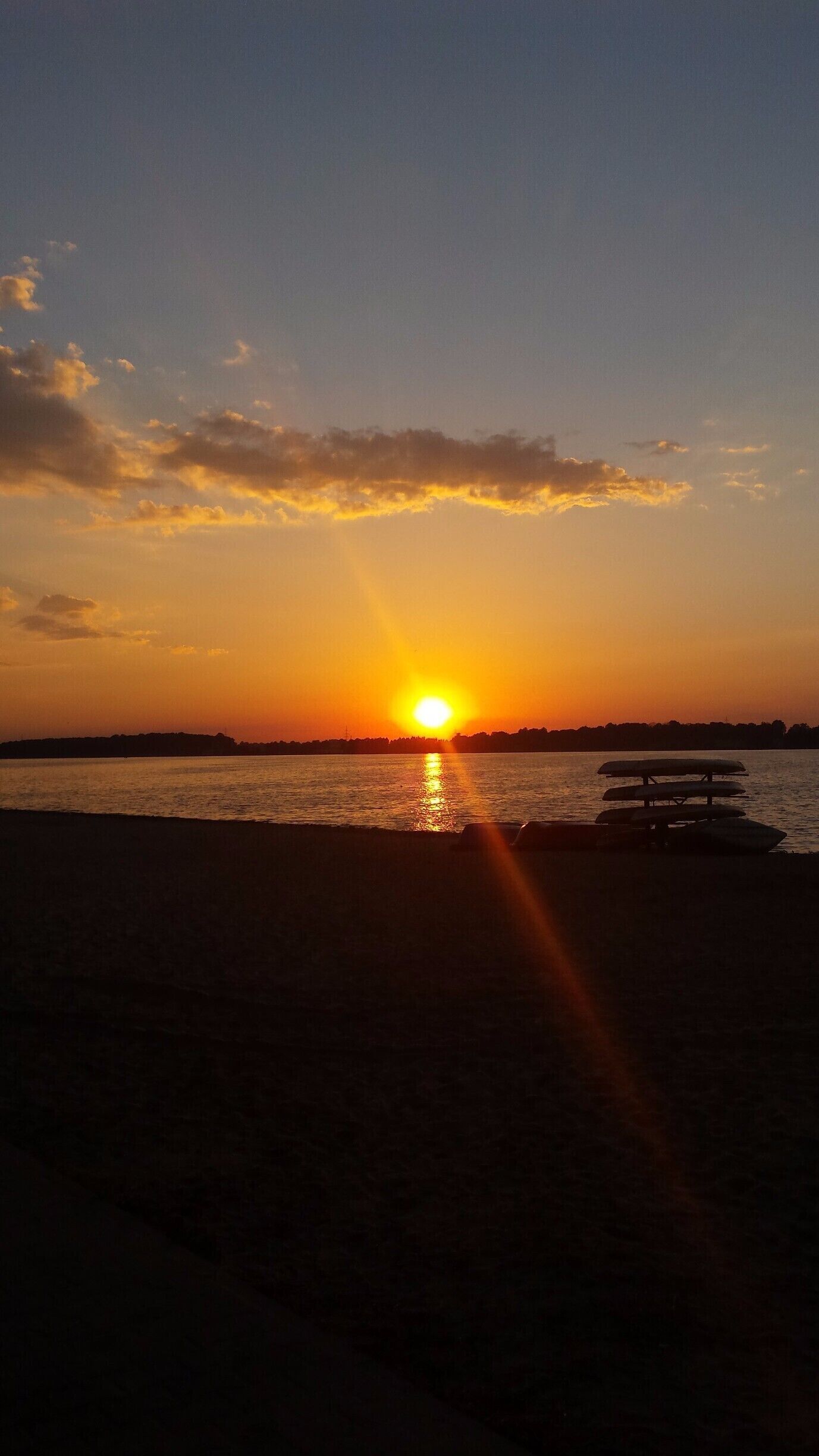 A sunset over a body of water with a bench in the foreground.