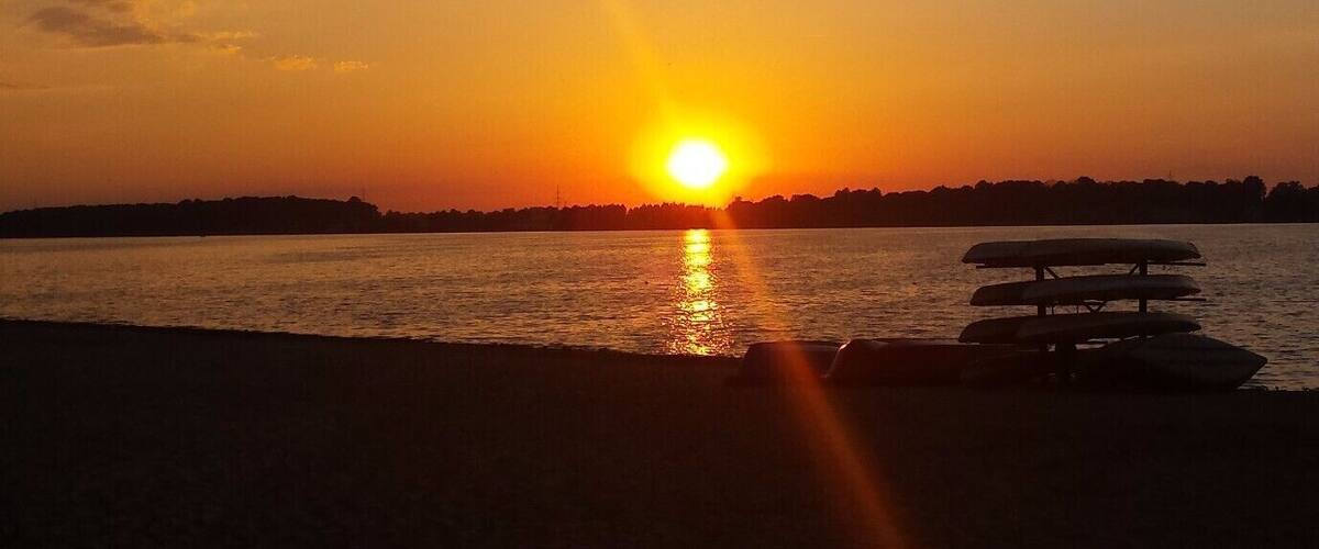 A sunset over a body of water with a bench in the foreground.