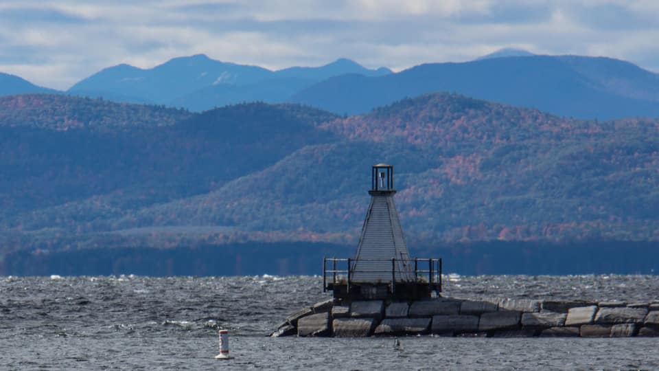 A lighthouse on a rocky outcrop with mountains in the background.