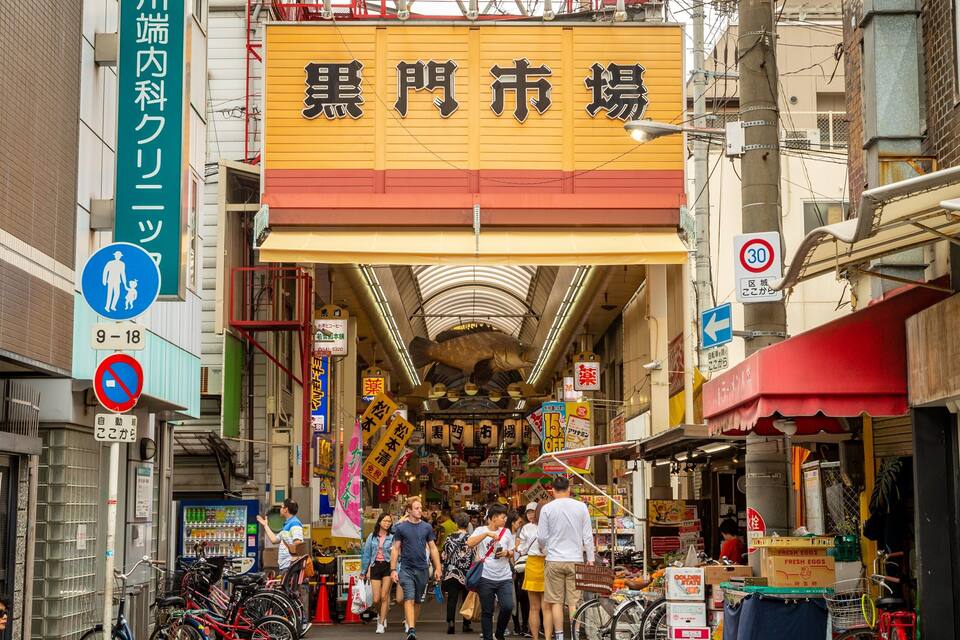 A busy street with a yellow sign reading "Black Market" and various shops and people.