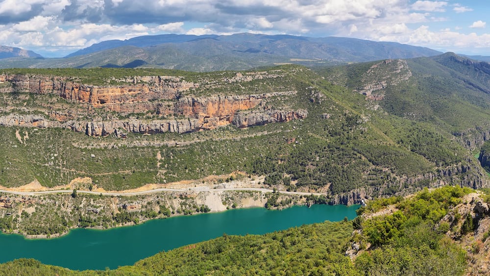 Eine Berglandschaft mit einem türkisblauen See, grünen Wäldern und felsigen Klippen.