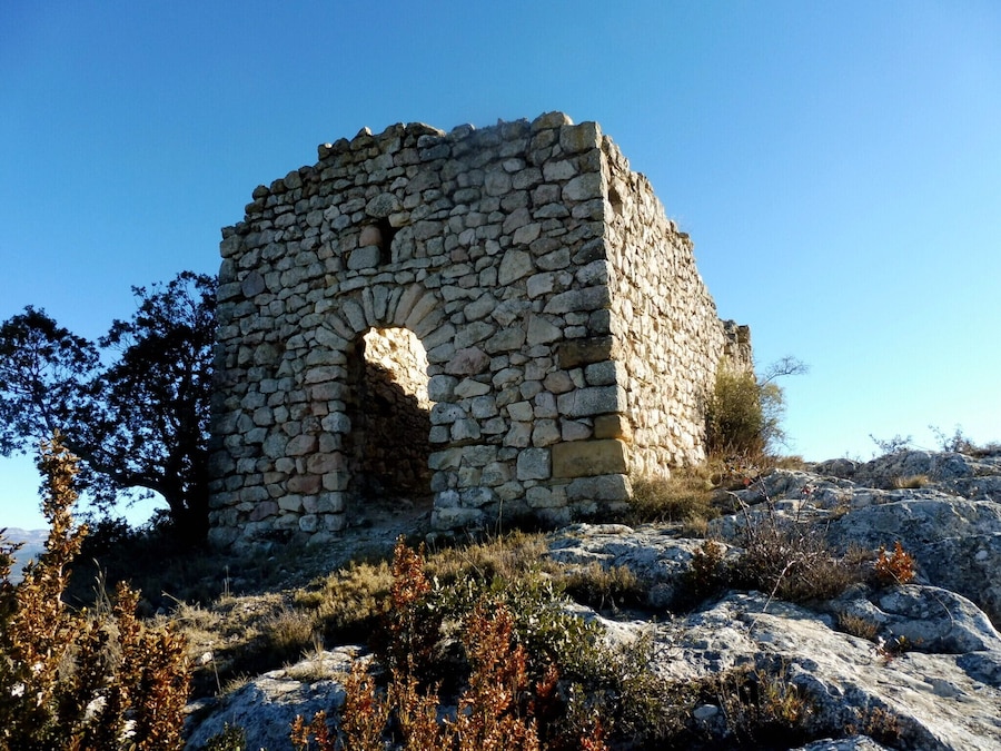 Una torre de piedra con una ventana arqueada central, rodeada de terreno rocoso y vegetación escasa.