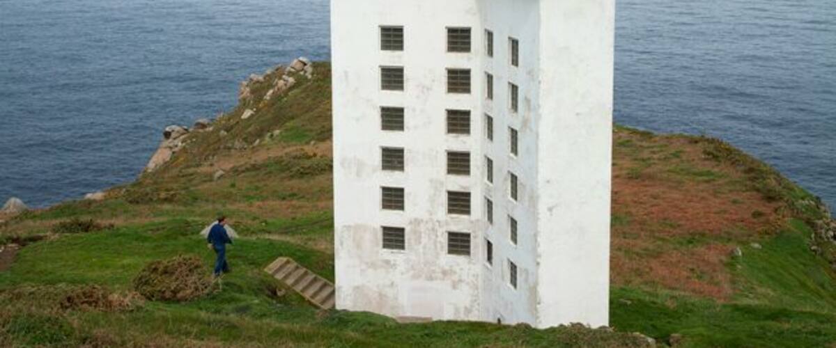 A white building with a red roof on a grassy cliff overlooking the sea.