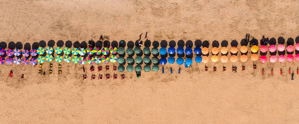 A beach with colorful umbrellas and beach chairs arranged in rows.