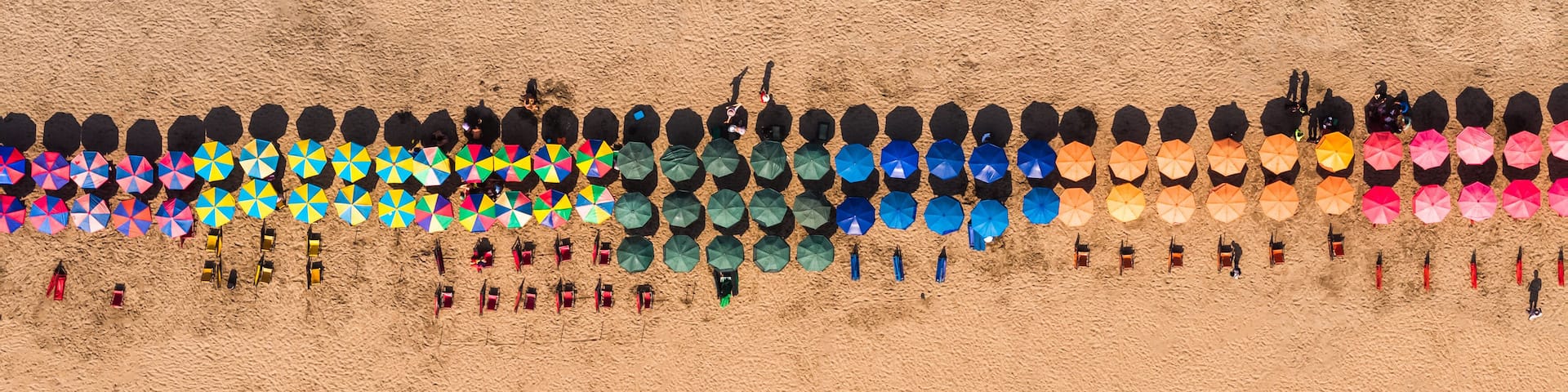 A beach with colorful umbrellas and beach chairs arranged in rows.