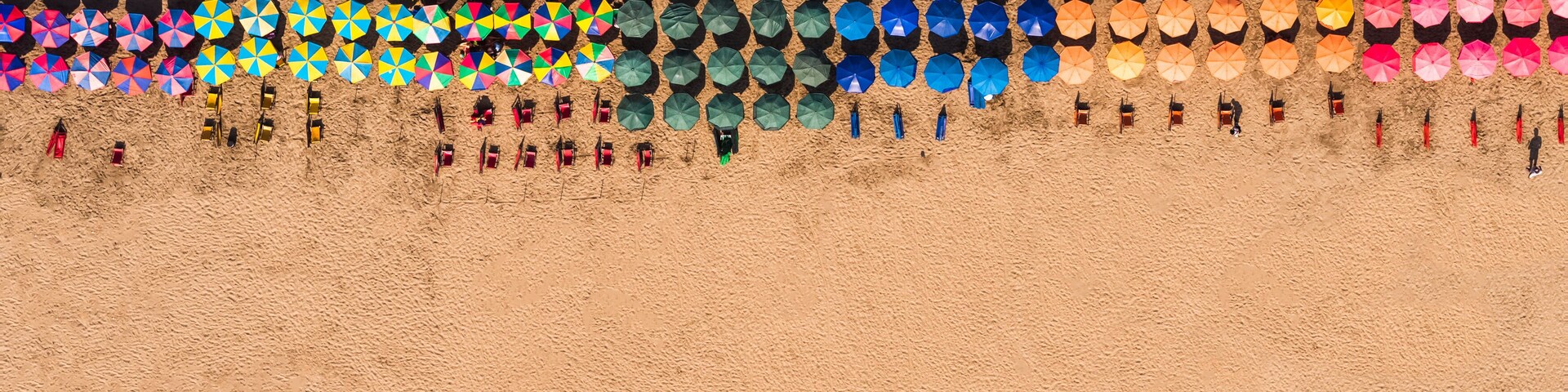 Una playa con sombrillas y sillas de playa de colores, dispuestas en filas.