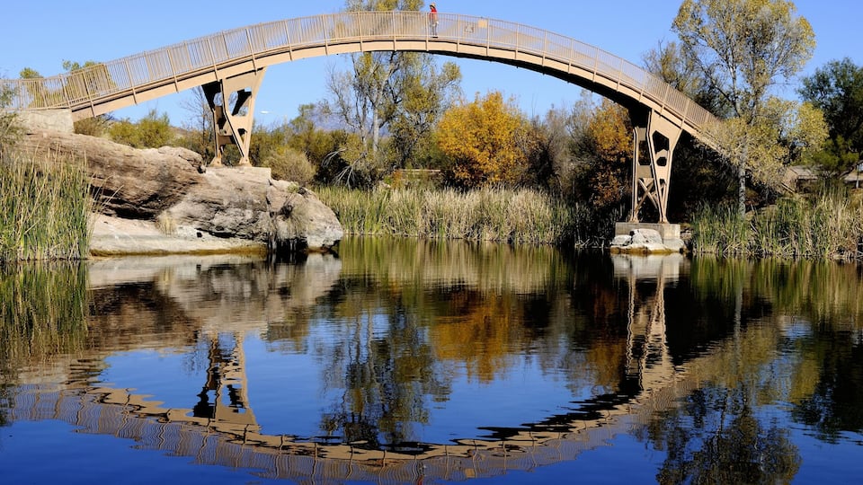 A wooden bridge over a calm river with clear reflections, surrounded by trees and rocks.