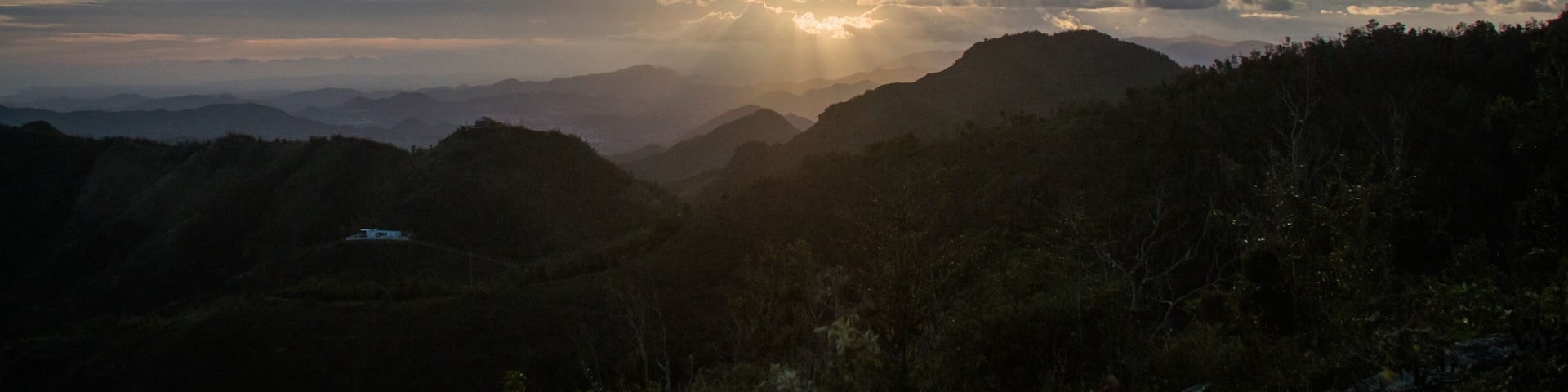 A sunrise over a mountainous landscape with a house on a hill.