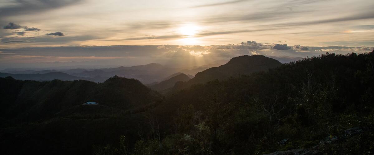 A sunrise over a mountainous landscape with a house on a hill.