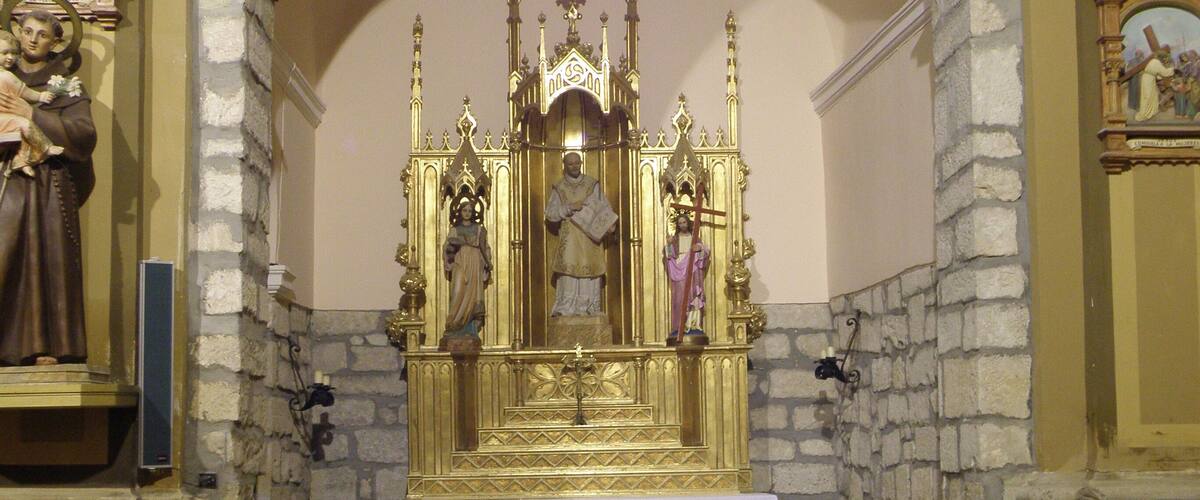 An interior of a church with a golden altar, stone walls, and wooden benches.