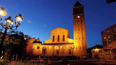 A church with a tall bell tower and a dome, illuminated by street lamps.