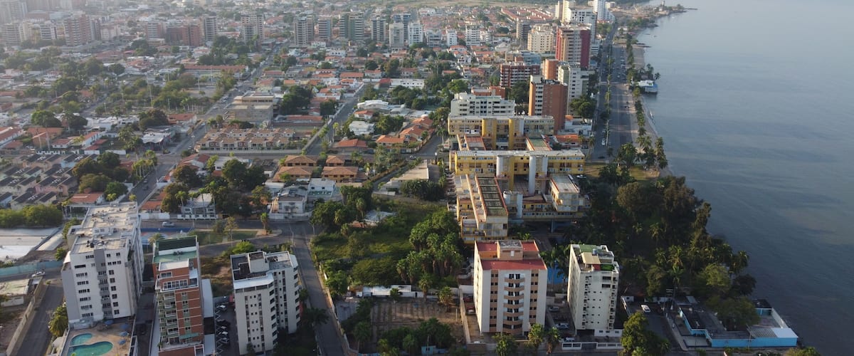 An aerial view of a coastal city with dense urban development, a prominent waterfront, and a mix of residential and commercial buildings.