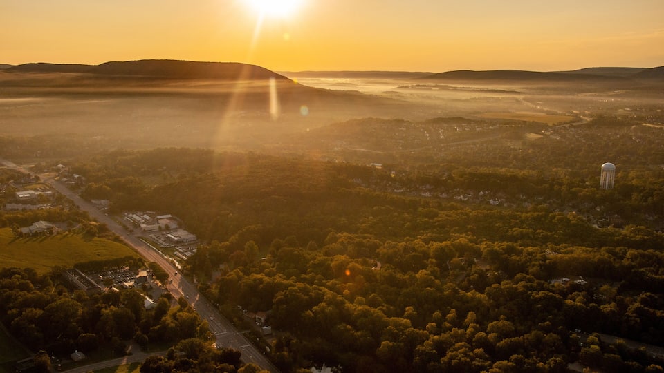 A sunrise over a valley with a water tower, roads, and scattered buildings.