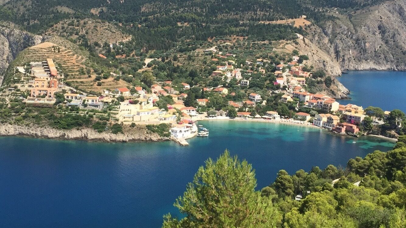 A coastal village with terraced houses, a clear blue sea, and a boat docked near the shore.