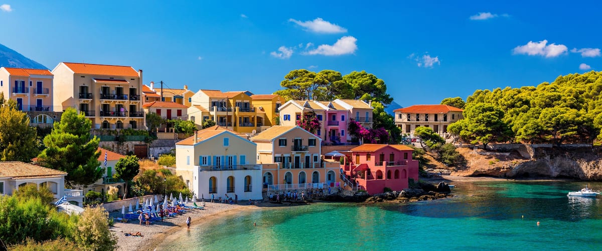 A coastal town with colorful buildings, a clear turquoise sea, and a rocky hillside.