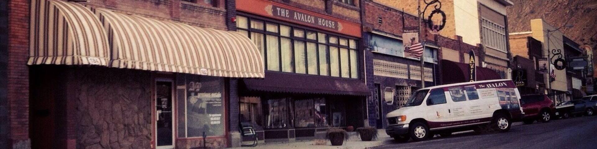A street with a row of brick buildings, including 'The Avalon House' with a striped awning.
