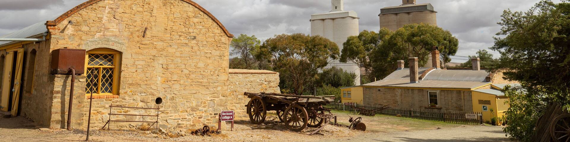 Un bâtiment en pierre avec une porte jaune, un chariot en bois et, au fond, des silos qui se dressent.
