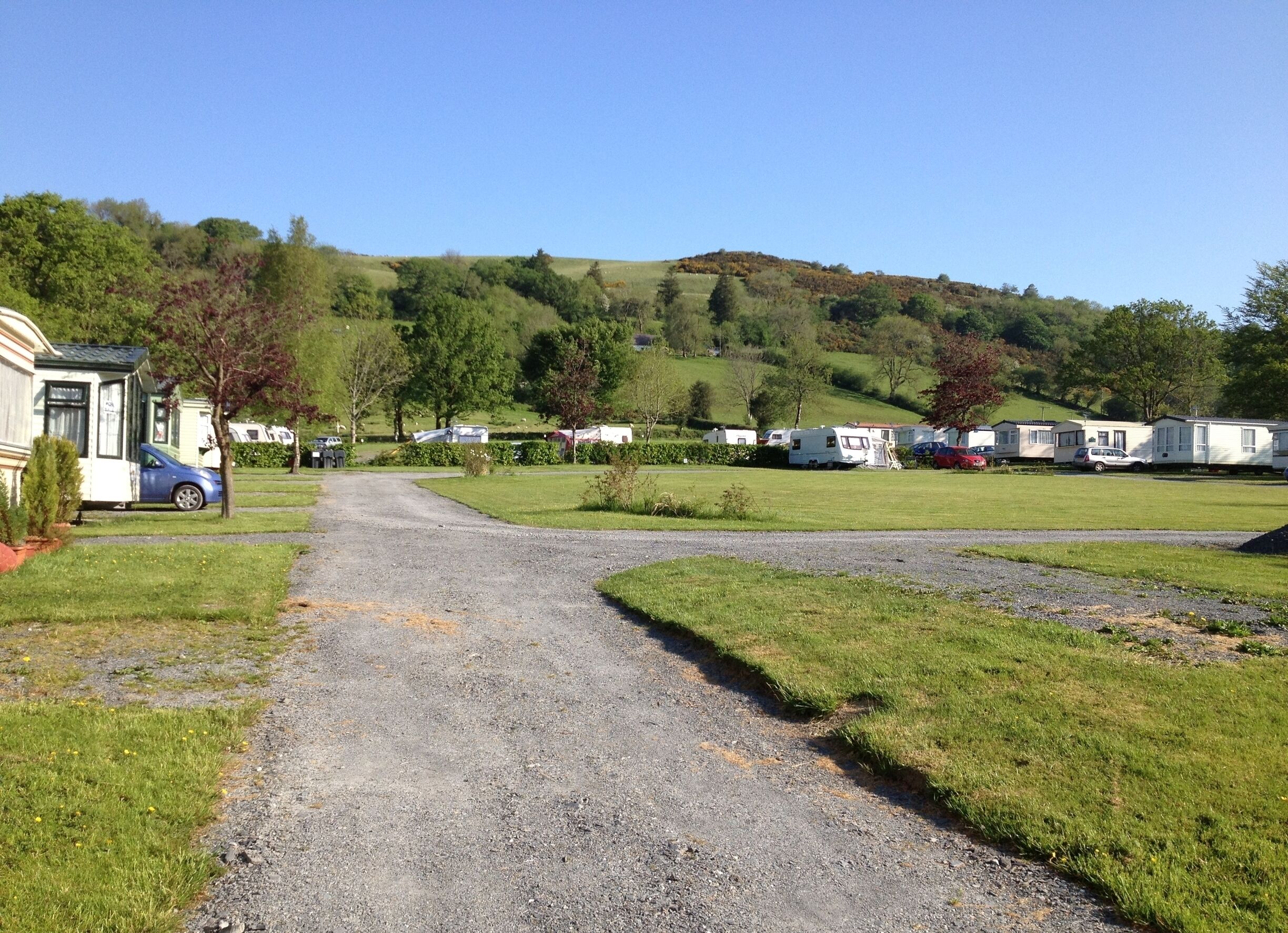 A gravel path leading to a caravan park with green hills in the background.