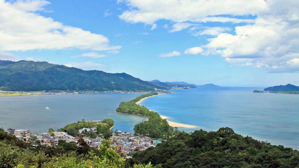 A coastal town with a bay, surrounded by mountains and a clear sky.