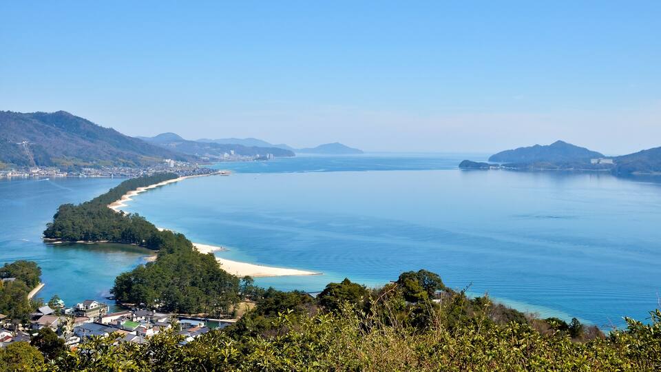 A coastal landscape with a bay, sandy beach, and surrounding hills.
