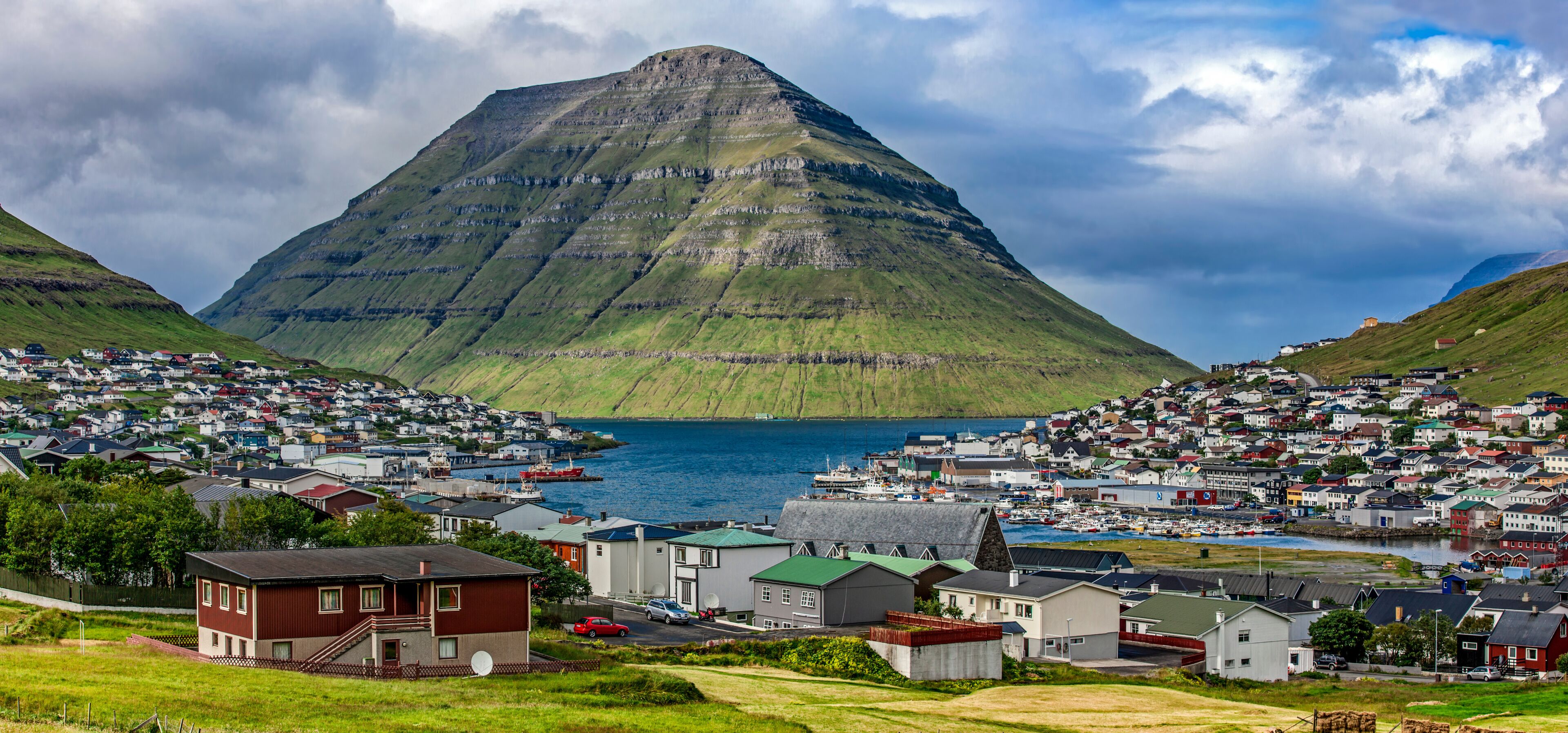 A coastal town with a prominent mountain in the background, a harbor with boats, and houses along the shoreline.