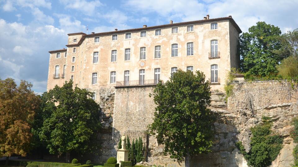 A historic stone building with multiple windows and a garden in front.