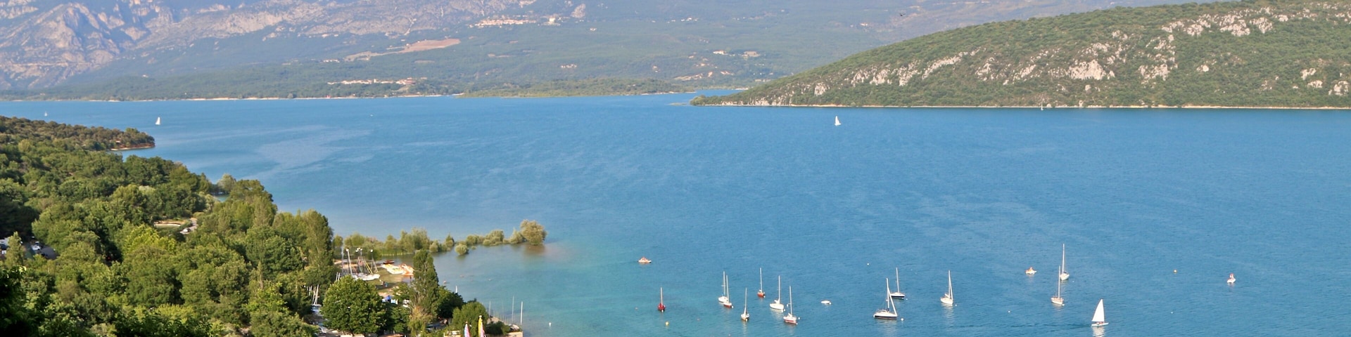 Un lago con veleros, rodeado de montañas y abundante vegetación.