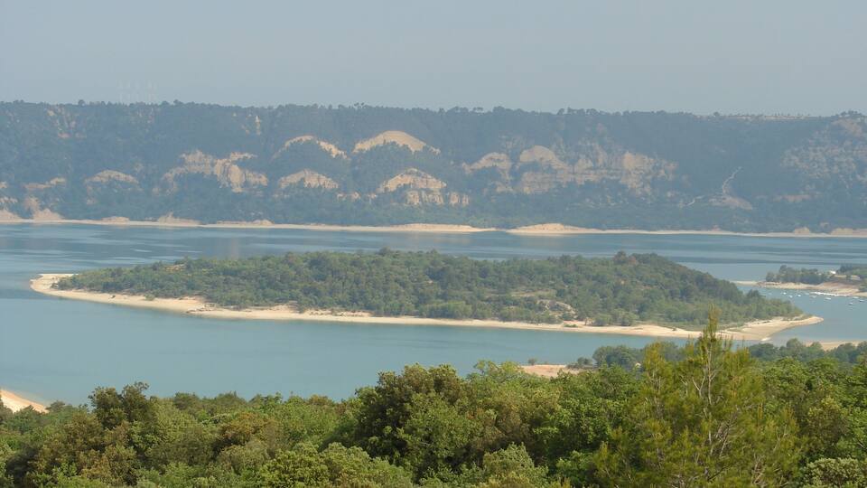 A coastal landscape with a sandy beach, a small island, and a forested hill in the background.