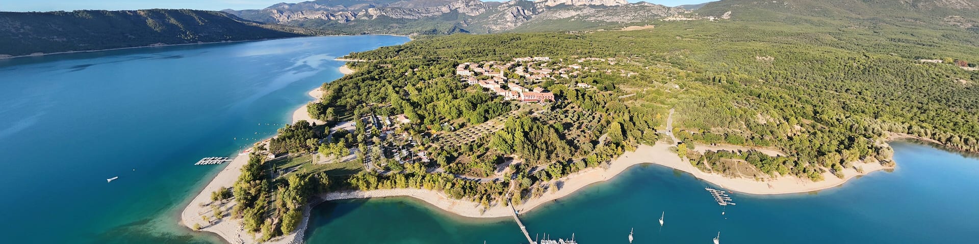 An aerial view of a coastal town with a marina, surrounded by mountains and a large body of water.