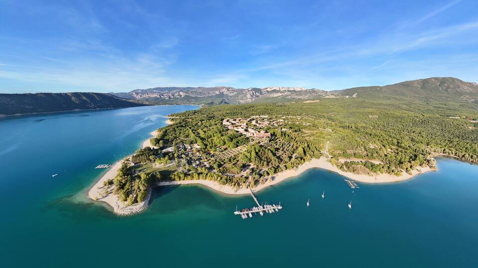 An aerial view of a coastal town with a marina, surrounded by mountains and a large body of water.