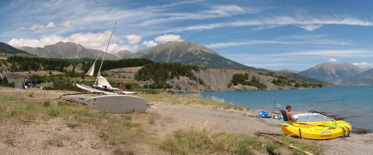 A lake with mountains in the background, a boat on the shore, and a person sitting on a chair.