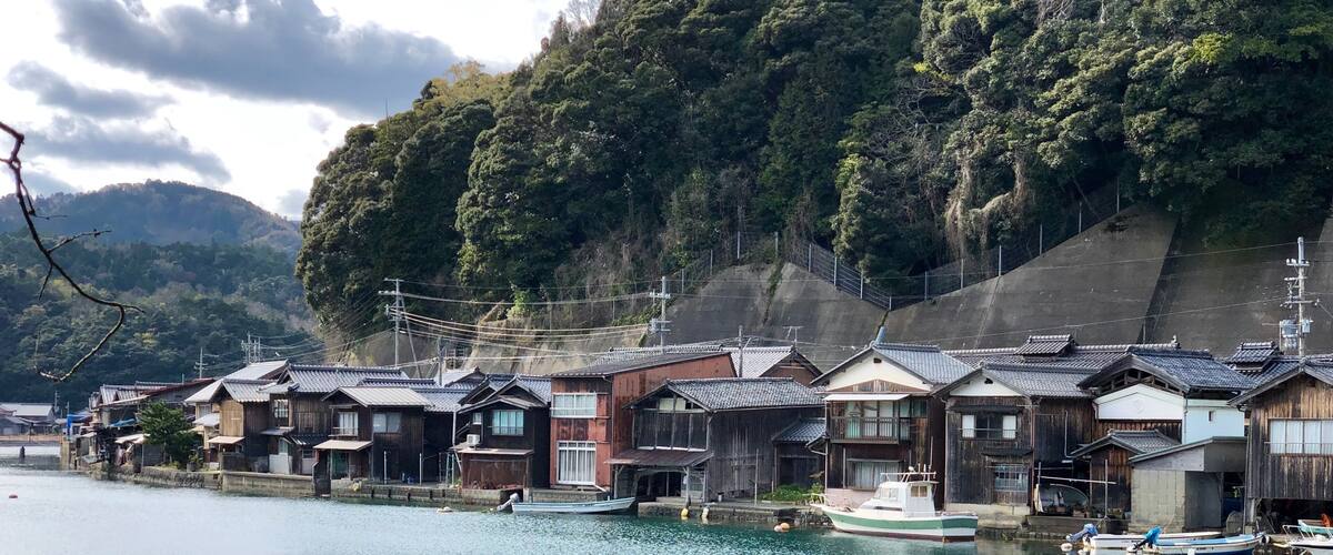 A traditional Japanese village by a calm river with wooden houses and boats.
