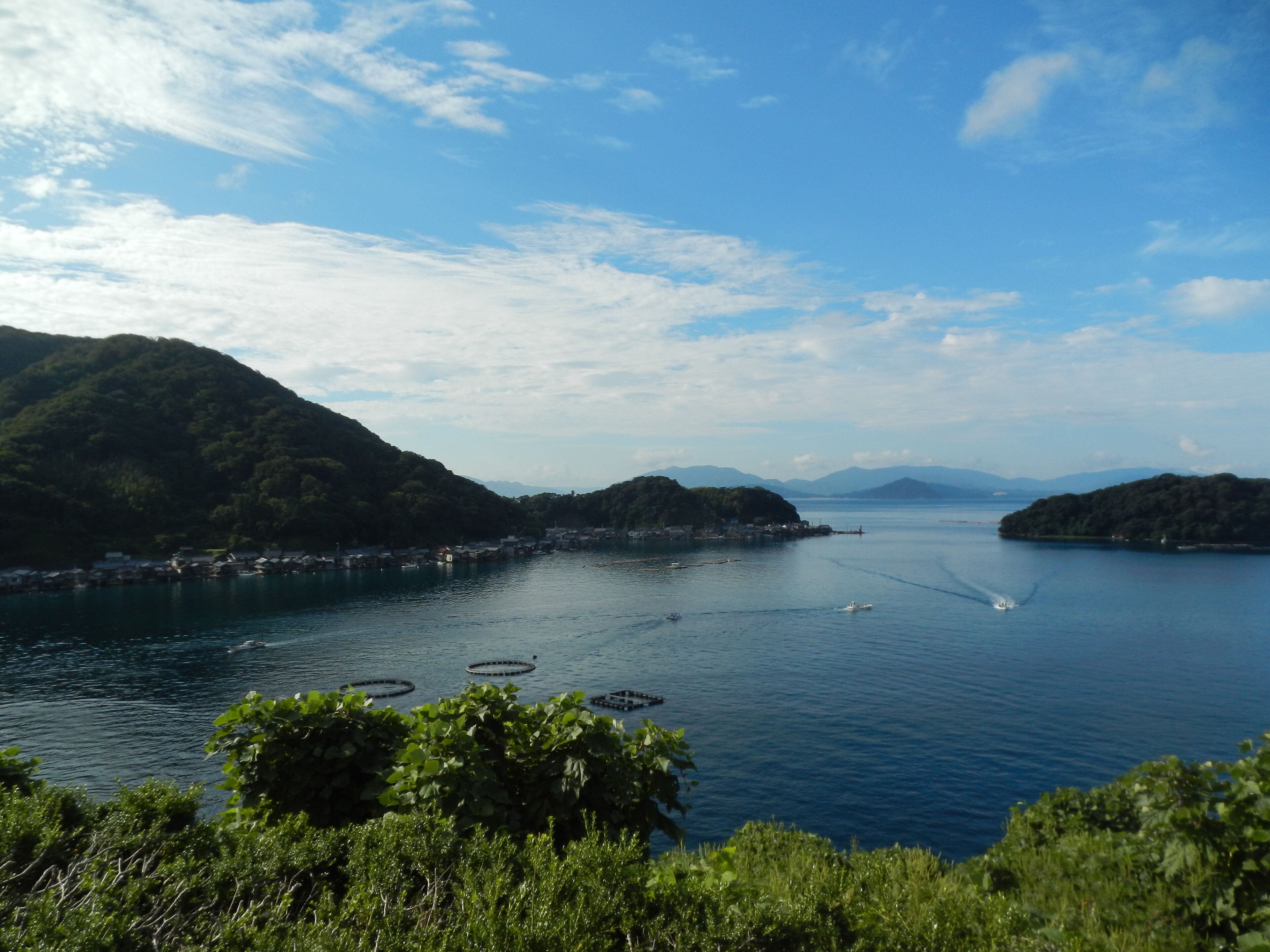 A coastal landscape with a clear sky, calm water, and lush green hills.