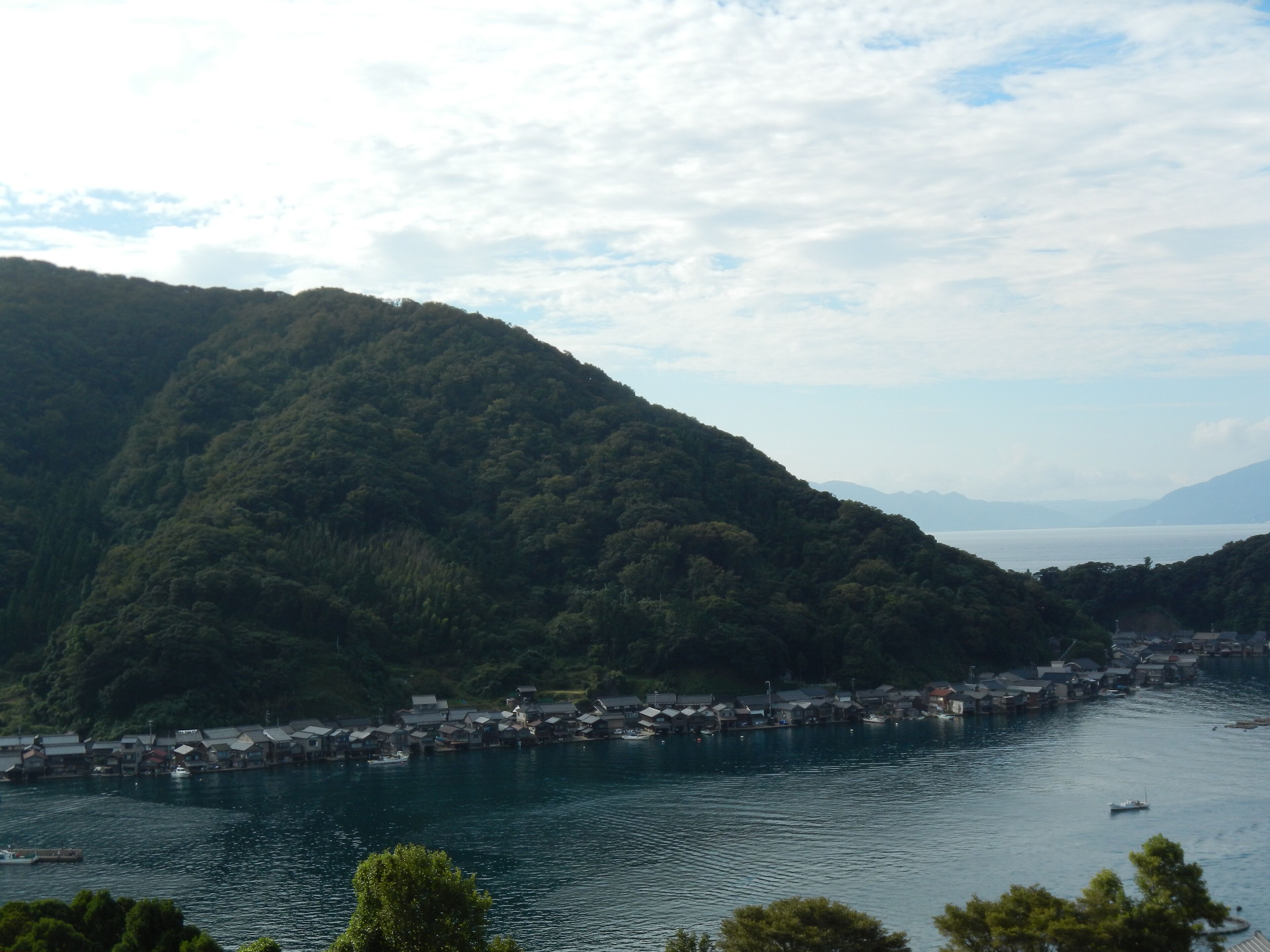 A coastal village with traditional houses by the sea, surrounded by lush green hills.