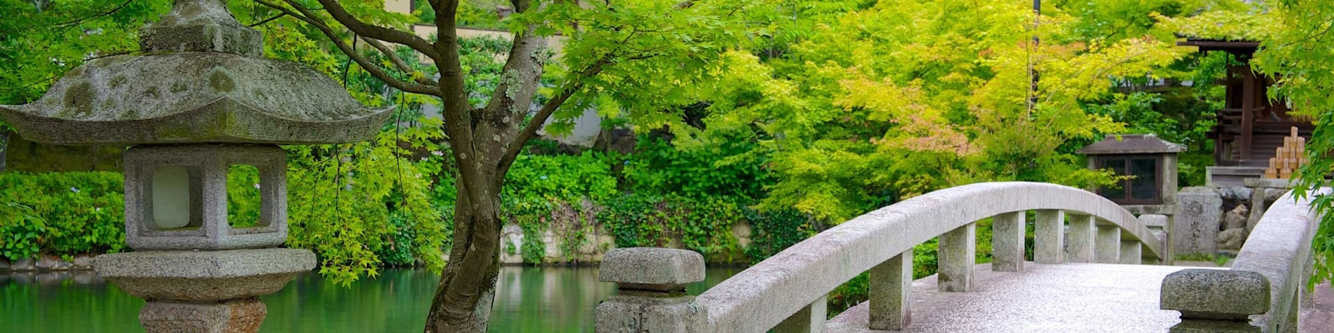 A stone bridge over a calm river, surrounded by lush greenery and traditional Japanese architecture.
