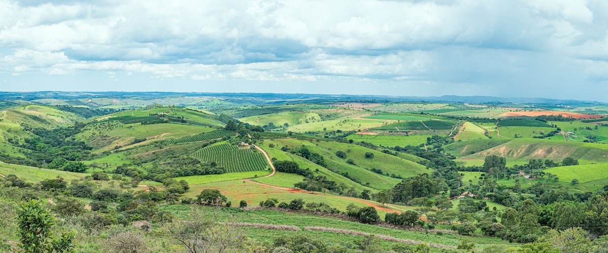 Rolling green hills, a winding road, and scattered buildings in a rural landscape.